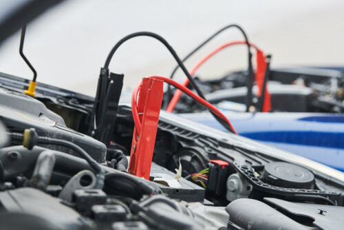 jumper cables attached to a car battery jumpstarting another car