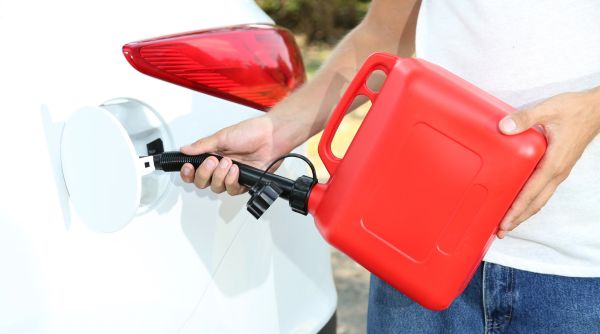 person with red gas tank filling car at the side of the road